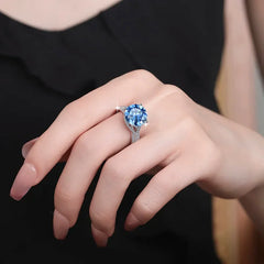 Hand wearing a ring with a blue gemstone against a black background