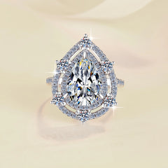 Elegant diamond ring with a pear-shaped center stone on a beige background