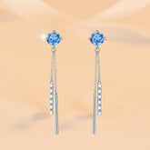 Pair of blue gemstone earrings with silver chains on a beige background