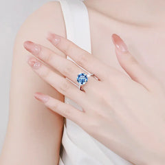 Close-up of a hand wearing a ring with a blue gemstone on a light background