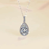 Teardrop-shaped diamond pendant on a chain against a soft beige background
