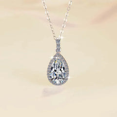 Teardrop-shaped diamond pendant on a chain against a soft beige background