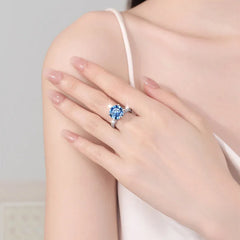 Close-up of a hand wearing a ring with a blue gemstone on a neutral background