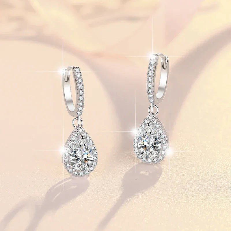 Teardrop-shaped silver earrings with clear gemstones on a soft beige background