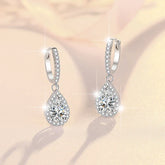 Teardrop-shaped silver earrings with clear gemstones on a soft beige background