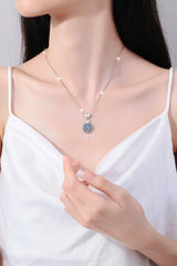 Woman wearing a silver necklace with a blue pendant against a neutral background