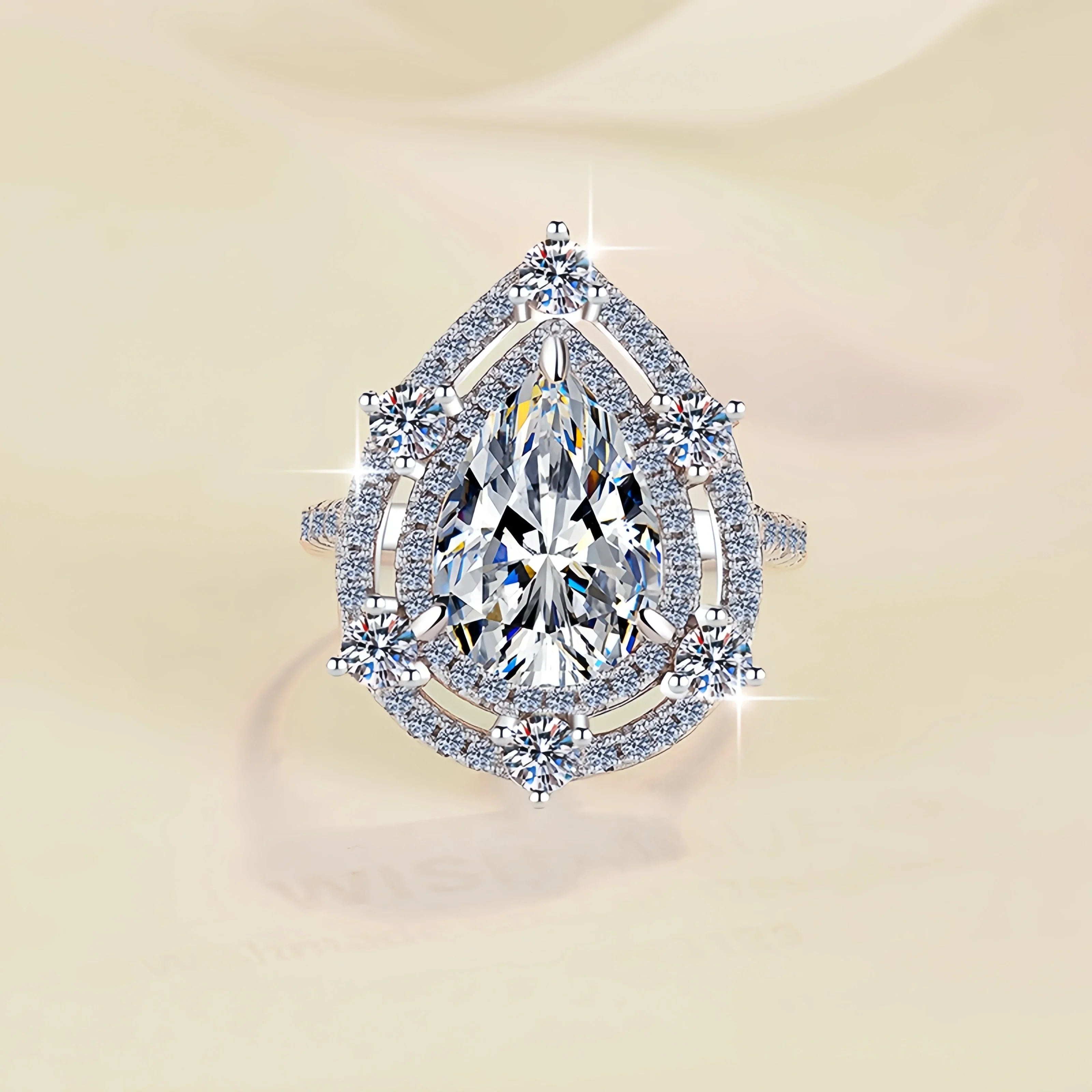 Elegant diamond ring with a pear-shaped center stone on a beige background