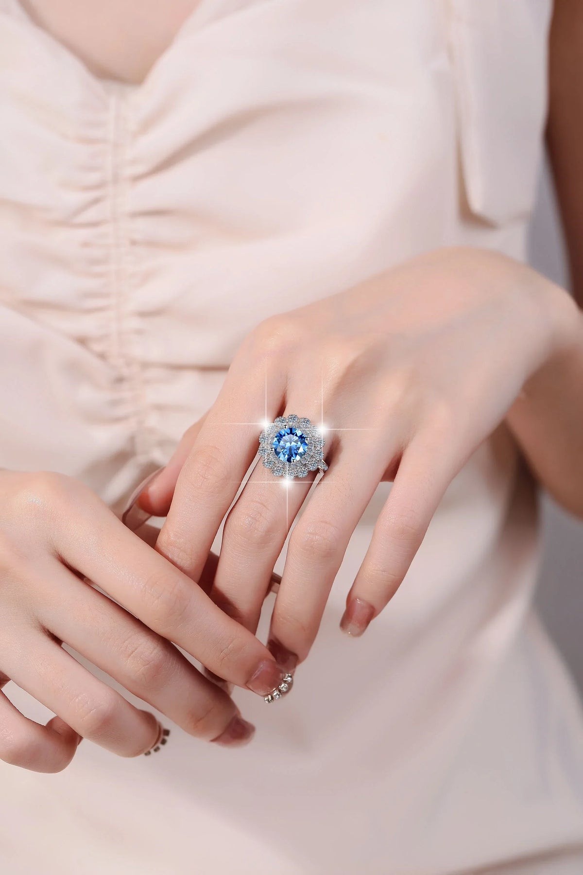 Close-up of a hand wearing a ring with a blue gemstone on a light background