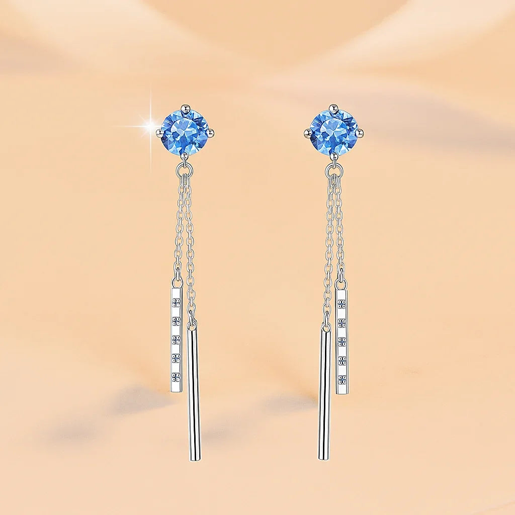 Pair of blue gemstone earrings with silver chains on a beige background