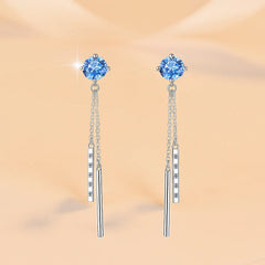 Pair of blue gemstone earrings with silver chains on a beige background