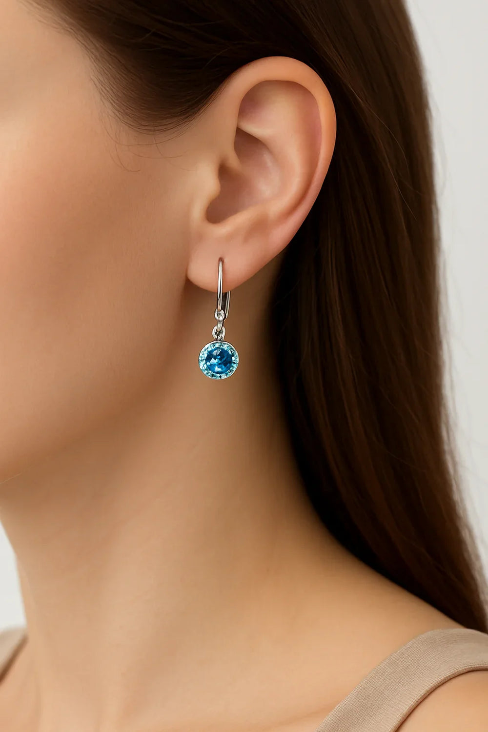 Close-up of a person wearing a blue gemstone earring with a neutral background