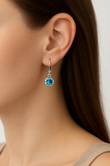 Close-up of a person wearing a blue gemstone earring with a neutral background