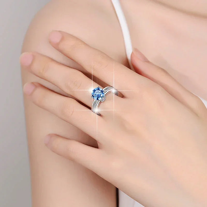 Close-up of a hand wearing a silver ring with a blue gemstone on a neutral background