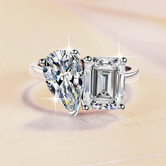 Diamond ring with pear-shaped and emerald-cut diamonds on a beige background
