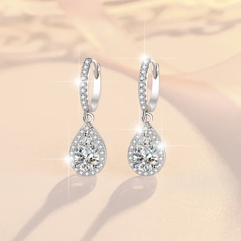 Pair of silver teardrop earrings with clear gemstones on a soft beige background