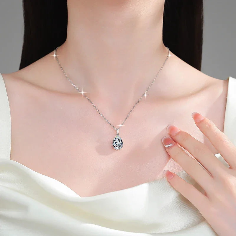 Silver necklace with a heart-shaped pendant worn by a model, with a hand touching the necklace.