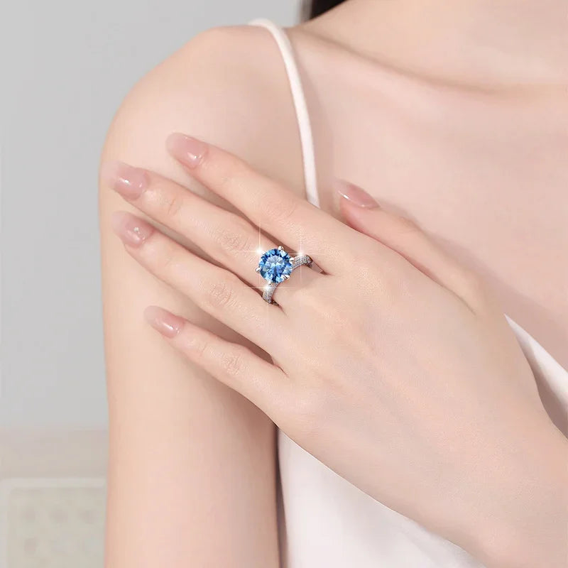 Close-up of a hand wearing a ring with a blue gemstone on a neutral background