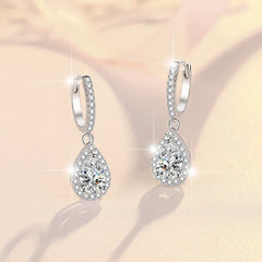 Teardrop-shaped silver earrings with clear gemstones on a soft beige background