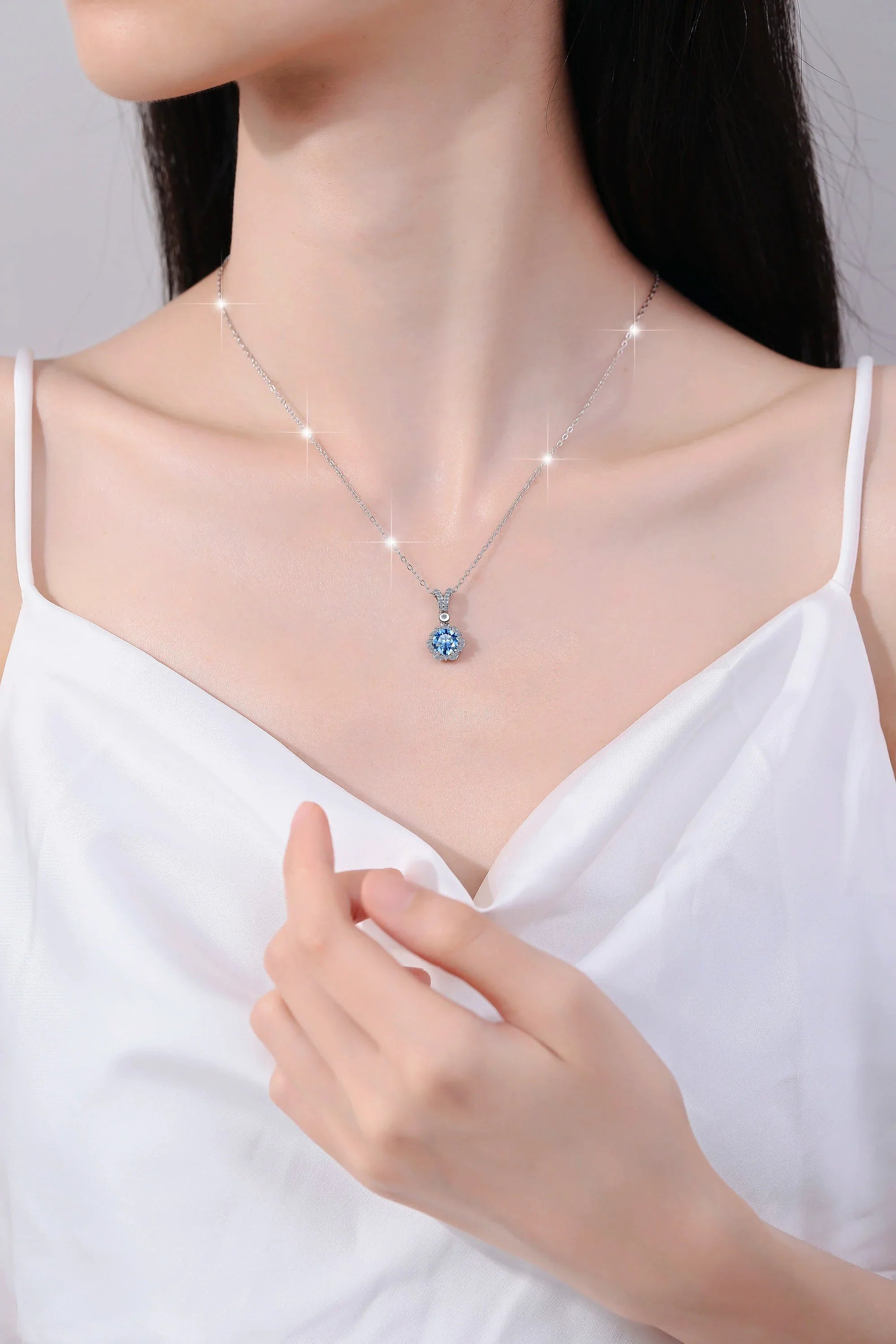 Necklace with a blue pendant worn by a person in a white top against a neutral background