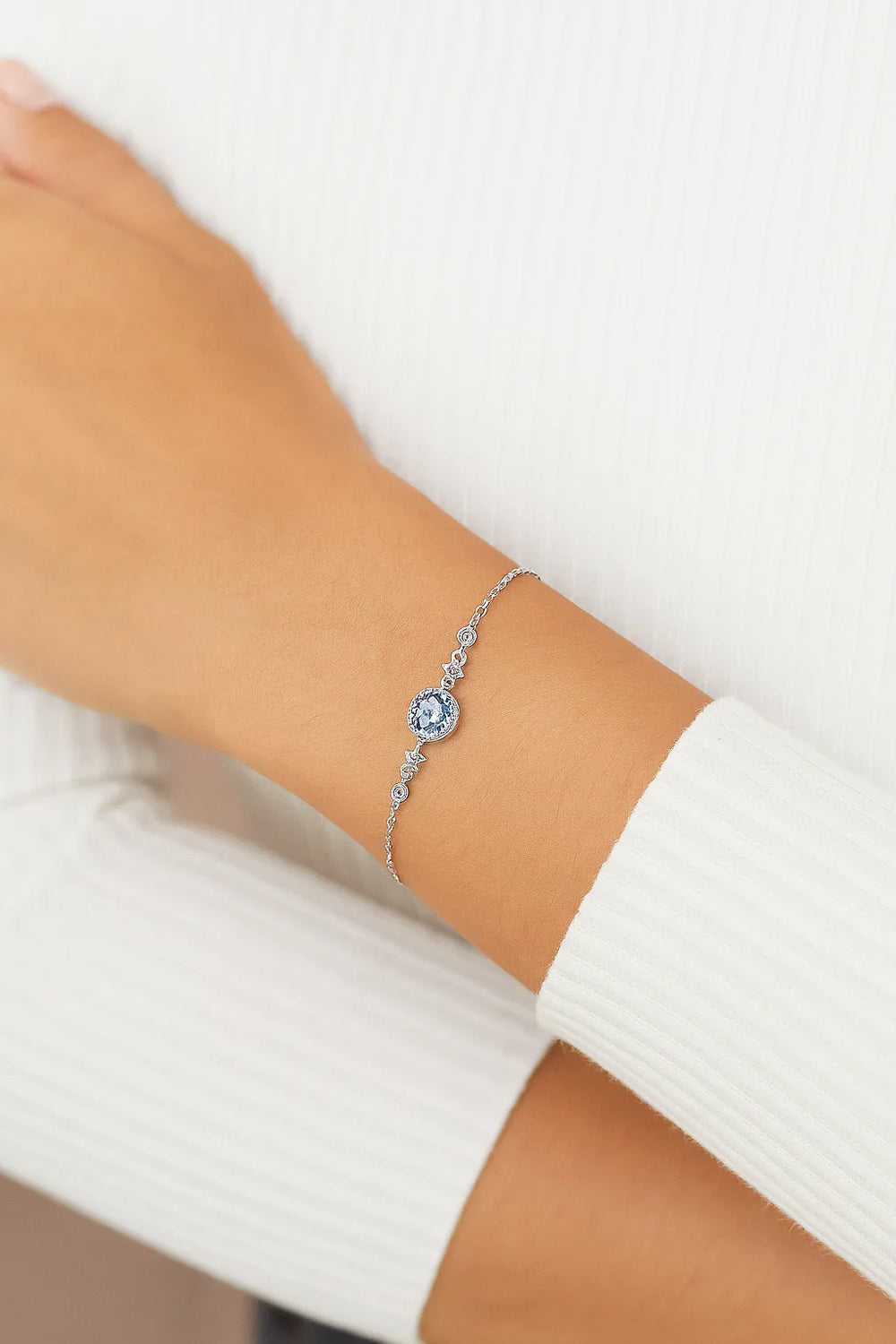 Silver bracelet with a blue gemstone on a wrist against a white background
